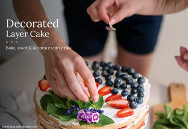 Baker decorating a layered sponge cake with fresh blueberries, strawberries, and edible flowers.