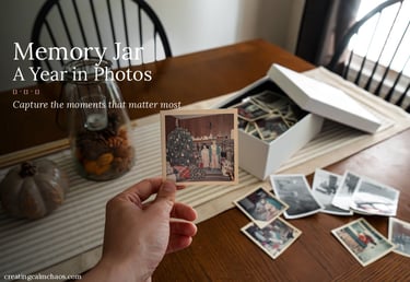 A hand holding a vintage polaroid photo over a table with a memory jar and photo storage box.