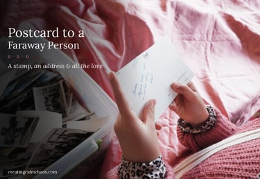 A person holding a handwritten vintage postcard over a box of old family photos on a pink bedspread.