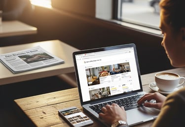 Young woman on a laptop in a coffee shop, with a newspaper in the background.