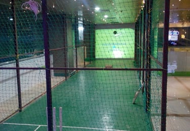 Indoor cricket practice net with a green turf floor and simulator screen for training.