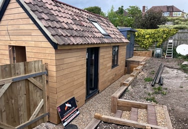 Side exterior of Brighton garage conversion with sweet chestnut cladding, black doors and oak retain