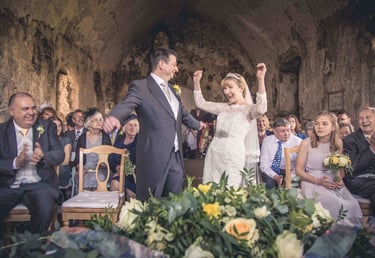 A joyful bride and groom celebrating their wedding ceremony inside a historic rustic chapel with guests.