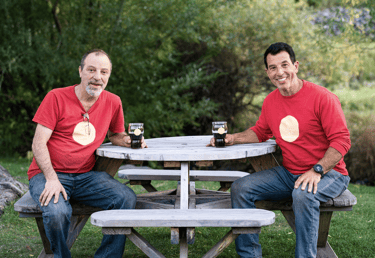 The Prairie Dog Tapproom owners, Jimmy and Michael Chidiac at a creekside table, toasting craft beer