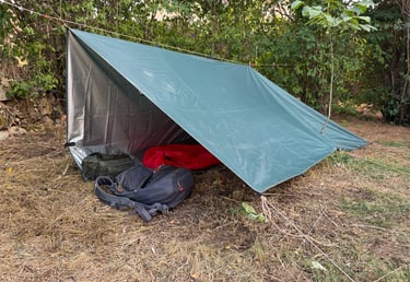 vista exterior de un refugio de fortuna construido con un tarp y línea de cordino