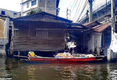 A local vendor in a small wooden boat selling goods at a Bangkok floating market canal.
