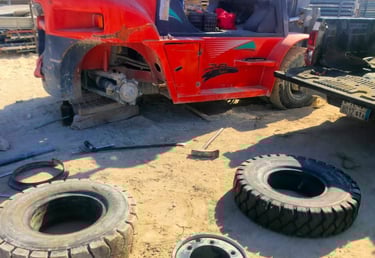 Red industrial forklift undergoing tire repair and maintenance at a sunny construction site.