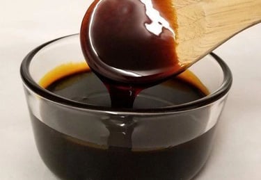 Thick balsamic glaze dripping from a wooden spoon into a glass bowl of dark balsamic vinegar sauce.