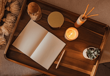 A wooden tray with an open notebook, pen, scented candle, and succulent for a cozy journaling setup.