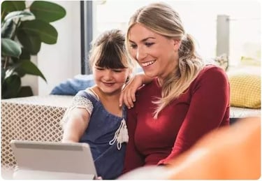 Smiling mother and young daughter using a tablet computer for remote learning or video calling at home.
