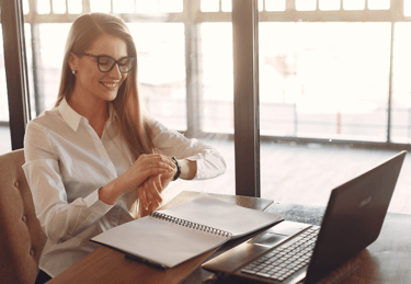 a woman sitting on her desk with a laptop and watching her time to indicate time management