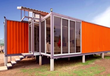 Modern orange shipping container home featuring glass walls and a raised foundation.
