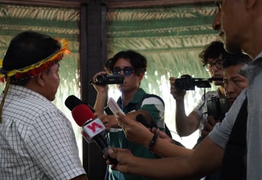 Indigenous leader in traditional headdress interviewed by journalists with microphones and cameras.