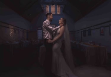 Smiling bride and groom embrace in a dimly lit, historic wedding reception hall with vaulted ceilings.