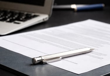 A silver ballpoint pen resting on a signed legal document or contract next to a laptop computer on a desk.
