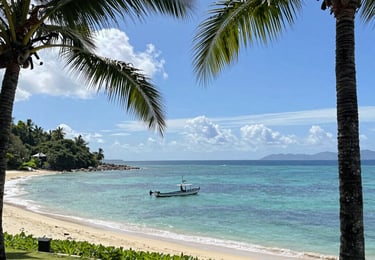 A stunning oceanfront villa with floor-to-ceiling windows overlooking the Kona coastline at sunset.