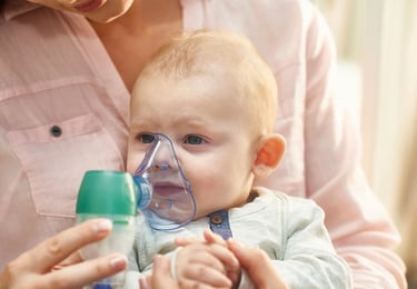 Mother holding baby using a nebulizer face mask for respiratory treatment of asthma or cold symptoms.