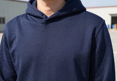 Close-up of a men's navy blue heavy-knit cotton hoodie texture, showing clean flatlock seams, bright natural daylight, 35mm