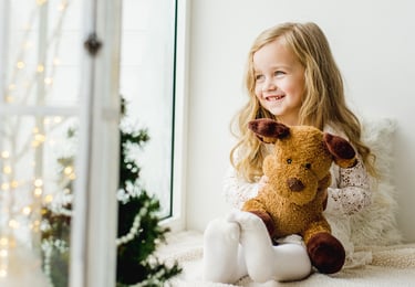 a little girl looking out the window sitting on a sofa with a teddy bear