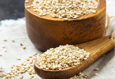 a wooden spoon with sesame seeds and a wooden bowl with sesame seeds