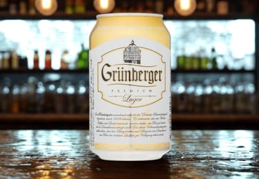 Can of Grünberger Premium Lager beer on a wooden bar counter with a blurred background.