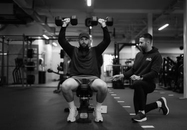"Personal trainer guiding client through seated shoulder press in Leamington gym, focusing on form and support.