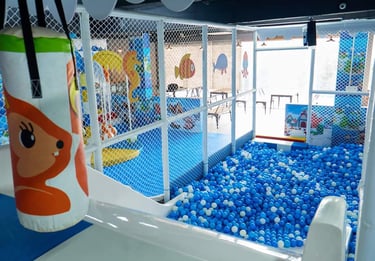 An indoor soft play area for children featuring a large ball pit with blue and white balls.