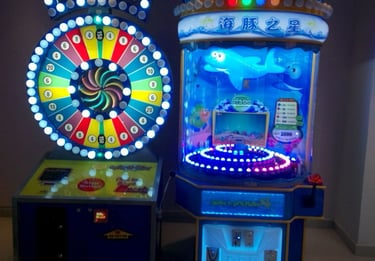 A colorful Spin-N-Win arcade wheel and Spin-A-Dolphin ticket redemption game glowing in a dark room.