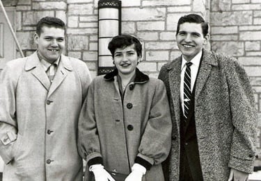 Vintage black and white photo of three young adults in formal coats and ties posing outdoors.