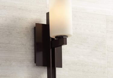 Modern dark bronze wall sconce with a cylindrical white frosted glass shade mounted on a tiled wall.