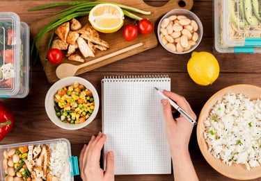 as mãos de uma pessoa segurando um caderno em uma mesa com frutas e fazendo anotações