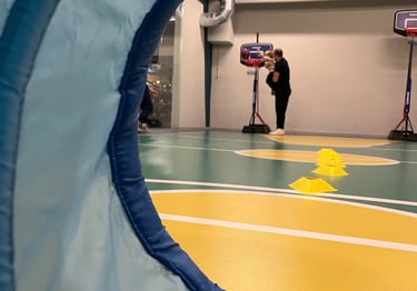 Vista attraverso un tunnel morbido in un'area multisport della palestra Move 2 Grow a Milano, con un adulto che aiuta un bamb