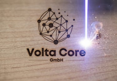 Precision laser engraving machine etching the Volta Core GmbH logo onto a wooden surface with sparks.