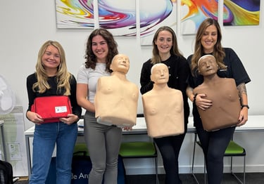 Group of first aid course learners standing with CPR training manikins after completing training