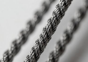 A close-up of high-tensile twisted yarn strands. The lighting is architectural, highlighting the spiral texture of the twist. Professional studio setting with a clean background.