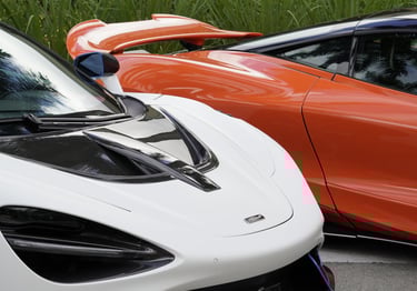 A white McLaren 765LT luxury supercar parked next to an orange McLaren exotic car on a city street.