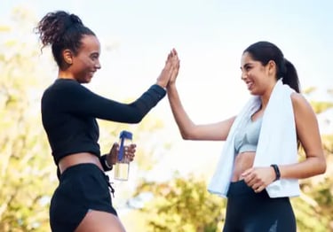Two smiling women in workout gear giving a high five after an outdoor fitness session.