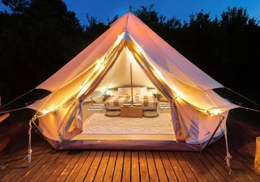 Luxury glamping bell tent at night with warm string lights, cozy interior bed, and wooden deck.