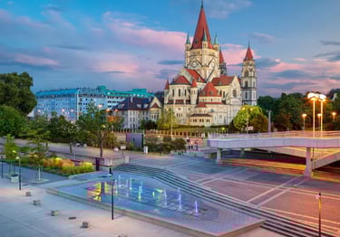 St. Francis of Assisi Church in Vienna, Austria, at sunset with a modern fountain and pink clouds.
