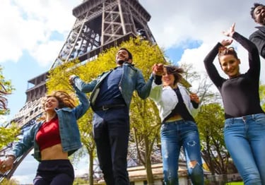 A diverse group of happy friends jumping and holding hands in front of the Eiffel Tower in Paris.
