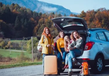 A happy family with luggage poses by their SUV during an autumn mountain road trip.