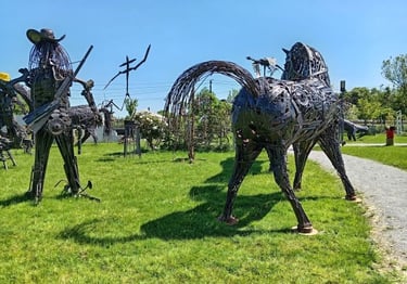 Handcrafted scrap metal sculptures of a horse and cowboy standing in an outdoor art garden.