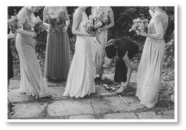Bridesmaids standing together while one is fixing her shoe strap.