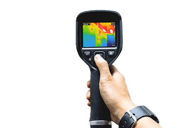 Hand holding an infrared thermal imaging camera displaying a heat map of a building interior.