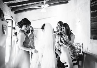 Fotografia in bianco e nero dei preparativi della sposa, mentre le amiche l'aiutano col velo dell'abito da sposa