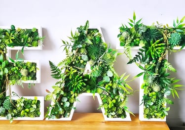 Decorative wall art spelling EAT using artificial succulents, moss, and green plants in white letter frames.