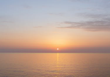 A soft sunrise over a calm sea, the sky shifting from darkness to light 