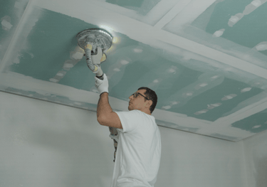 a man is painting a ceiling with a ceiling fan