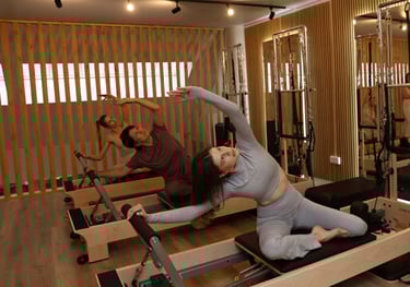 Três pessoas a fazer um alongamento lateral em reformers num estúdio de Pilates com espelhos 