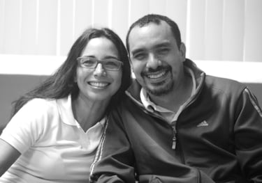 Un hombre y una mujer sentados uno junto al otro en un sofá, sonrientes miran la cámara